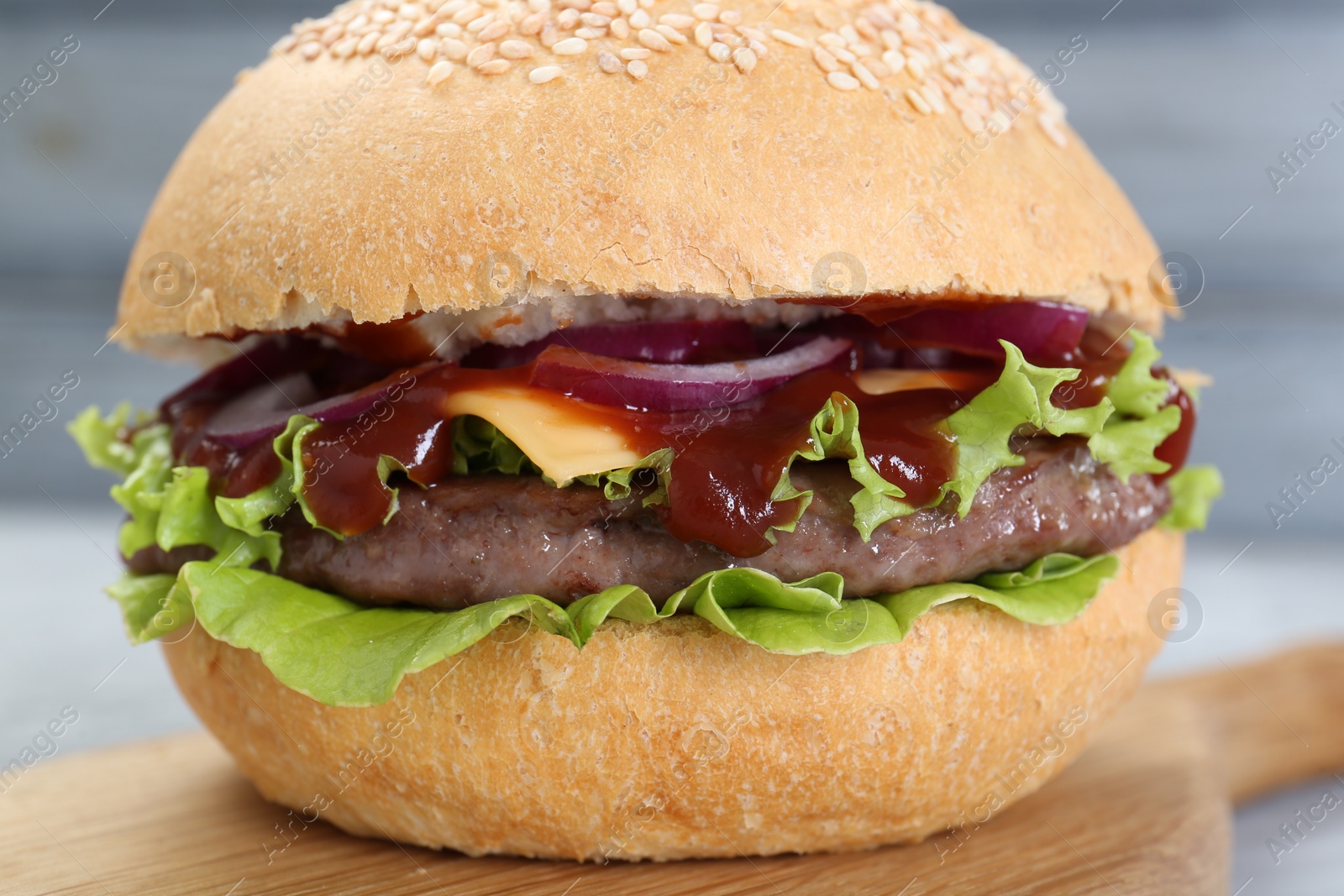 Photo of Delicious cheeseburger with lettuce, onion, ketchup and patty on blurred background, closeup