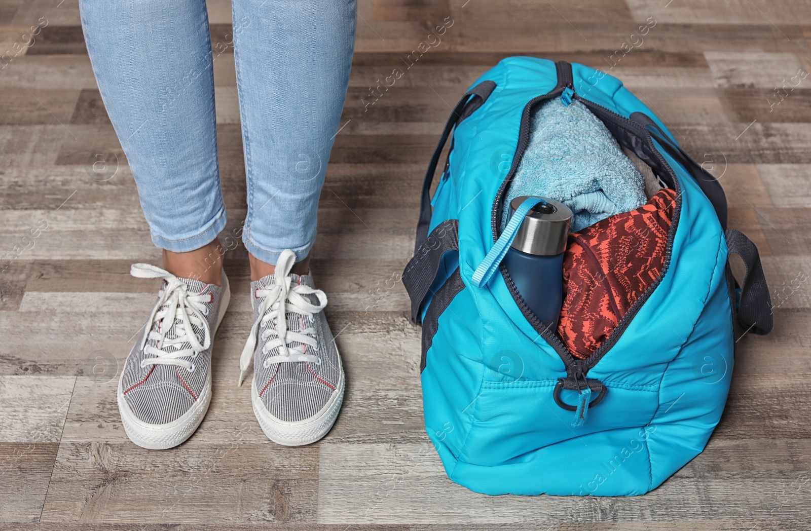 Photo of Young woman in sportswear and bag with gym equipment indoors