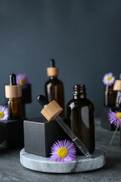 Photo of Bottles of essential oil and beautiful flowers on dark gray stone table