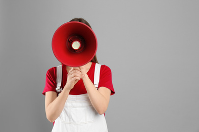 Photo of Young woman with megaphone on light grey background. Space for text