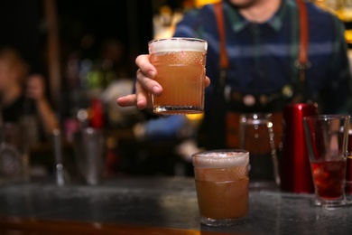 Photo of Bartender with glass of tasty cocktail at counter in nightclub, closeup