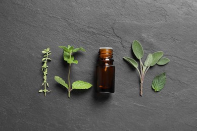 Photo of Bottle of essential oil, thyme, sage and mint on black table, flat lay