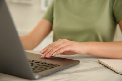 Photo of Woman working with modern laptop at marble table, closeup