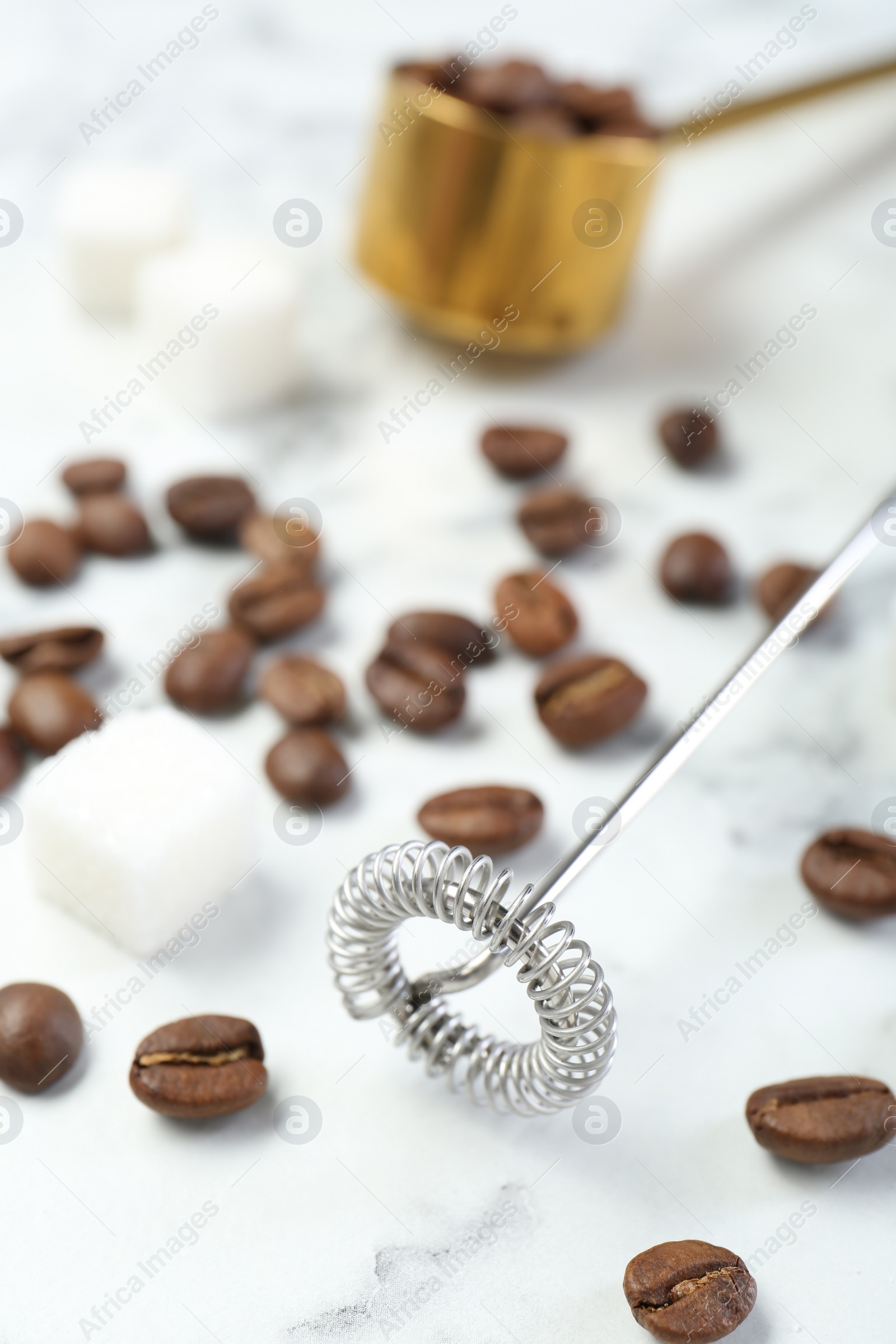 Photo of Milk frother wand, sugar cubes and coffee beans on white marble table, closeup