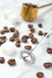 Milk frother wand, sugar cubes and coffee beans on white marble table, closeup