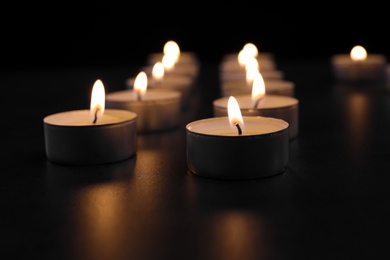 Photo of Burning candles on table in darkness, closeup. Funeral symbol