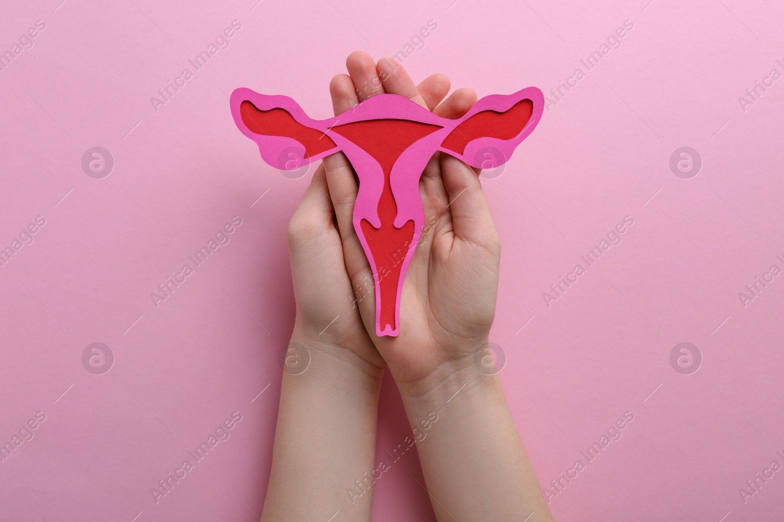 Photo of Reproductive medicine. Woman holding paper uterus on pink background, top view