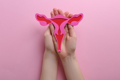 Photo of Reproductive medicine. Woman holding paper uterus on pink background, top view