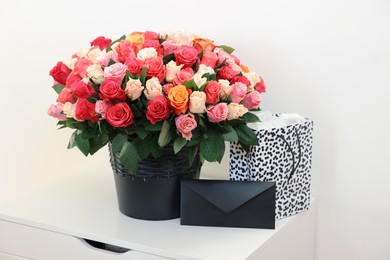 Photo of Bouquet of beautiful roses, envelope and shopping bag on white drawer unit