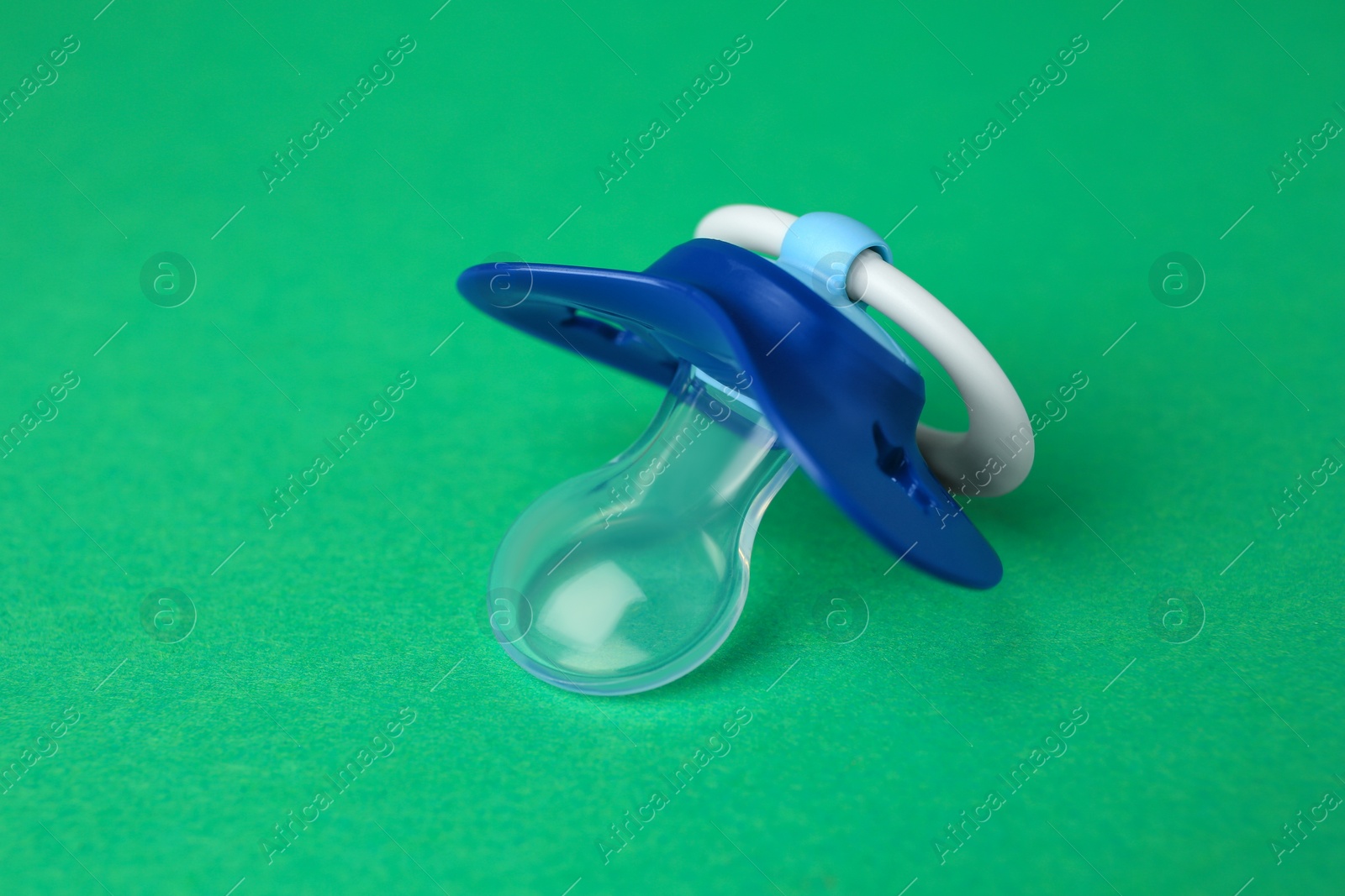 Photo of One blue baby pacifier on green background, closeup