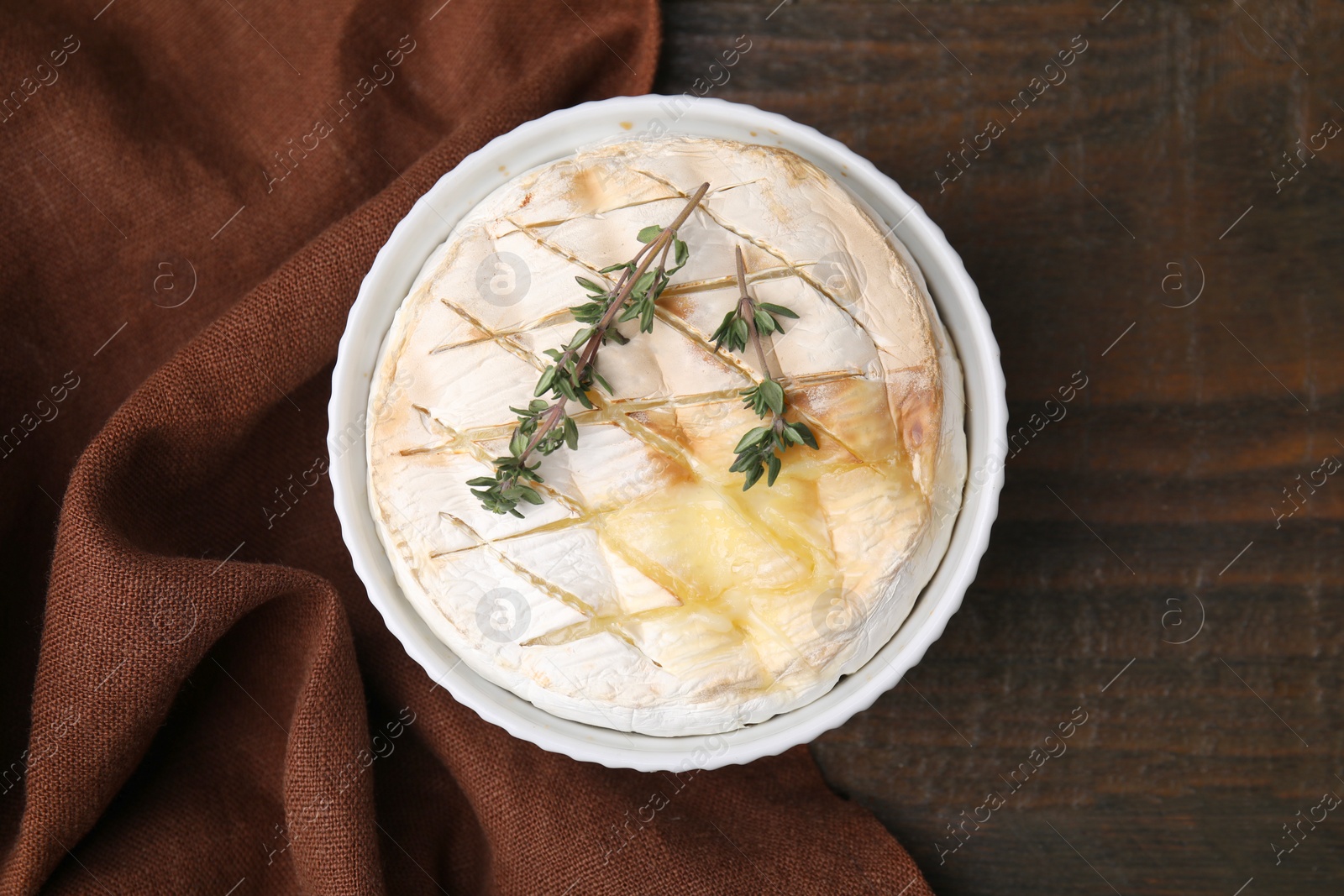 Photo of Tasty baked camembert and thyme in bowl on wooden table, top view