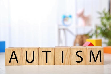 Photo of Wooden cubes with word AUTISM on table against blurred background