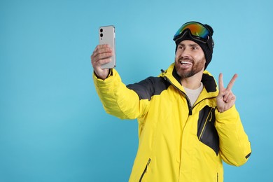 Photo of Winter sports. Happy man in ski suit and goggles taking selfie on light blue background
