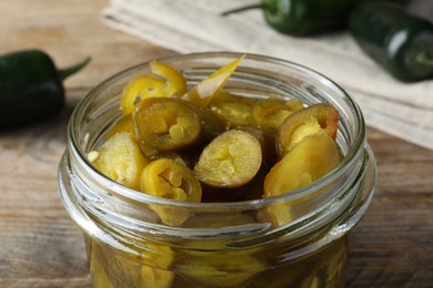 Photo of Glass jar with slices of pickled green jalapeno peppers on wooden table, closeup