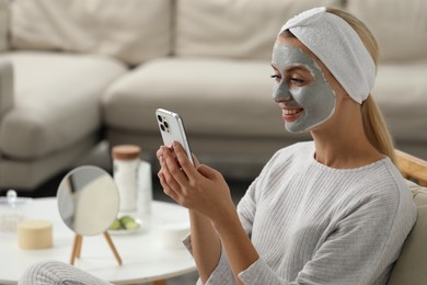Young woman with face mask using smartphone at home, space for text. Spa treatments