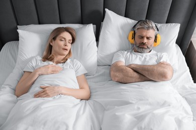 Photo of Irritated man with headphones lying near his snoring wife in bed at home