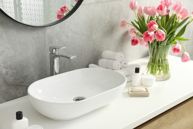 Photo of Vase with beautiful pink tulips and toiletries near sink in bathroom