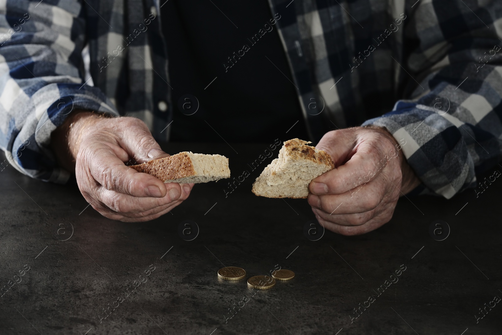 Photo of Poor elderly man with bread at table, focus on hands