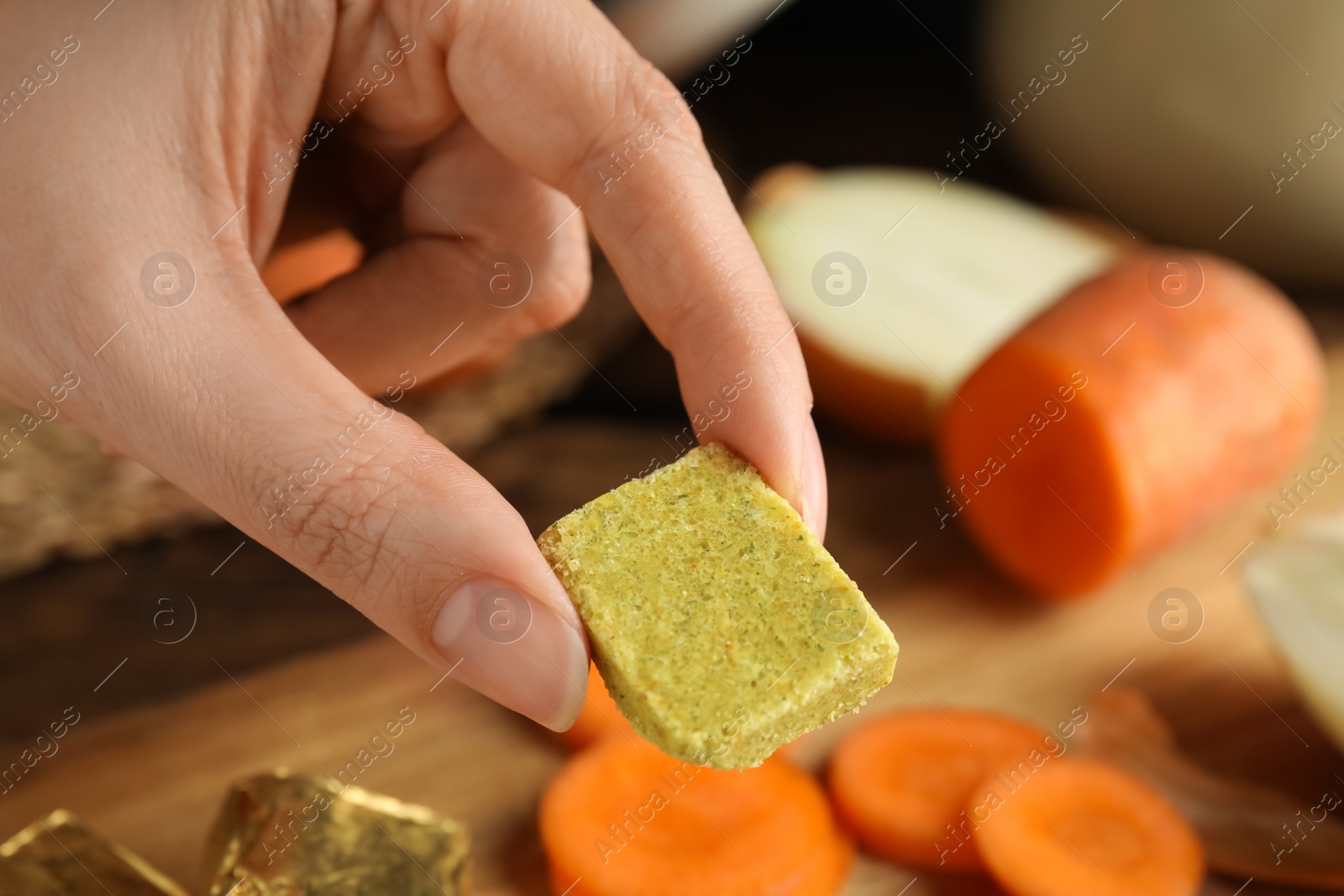 Photo of Woman holding bouillon cube at table, closeup