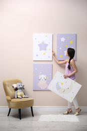 Photo of Decorator hanging pictures on pink wall. Children's room interior design