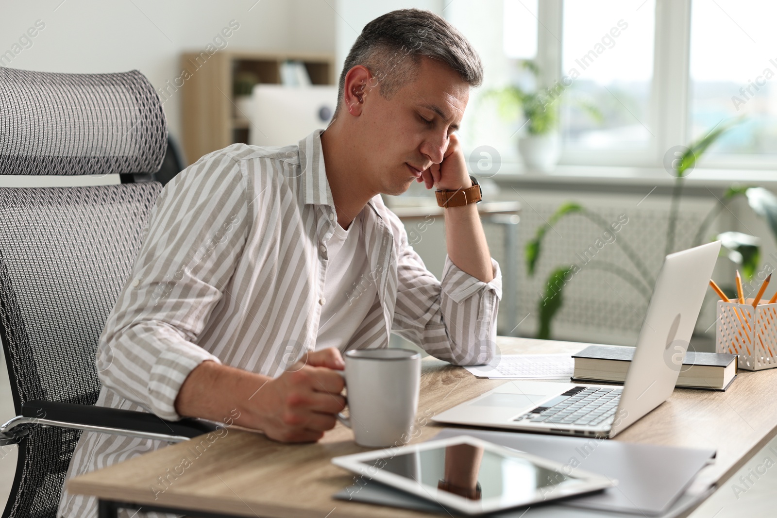 Photo of Man with cup of drink snoozing at wooden table in office