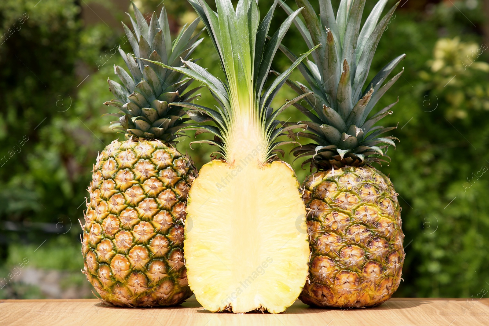 Photo of Delicious ripe pineapples on wooden table outdoors