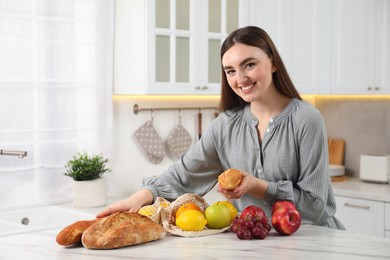 Woman with baguettes and string bag of fresh fruits at light marble table in kitchen