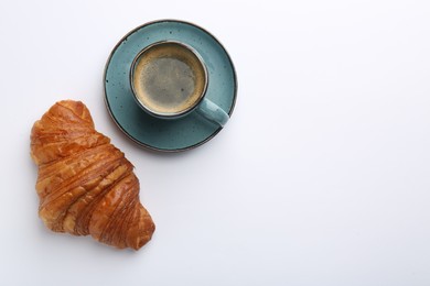 Delicious fresh croissant and cup of coffee on white background, flat lay. Space for text