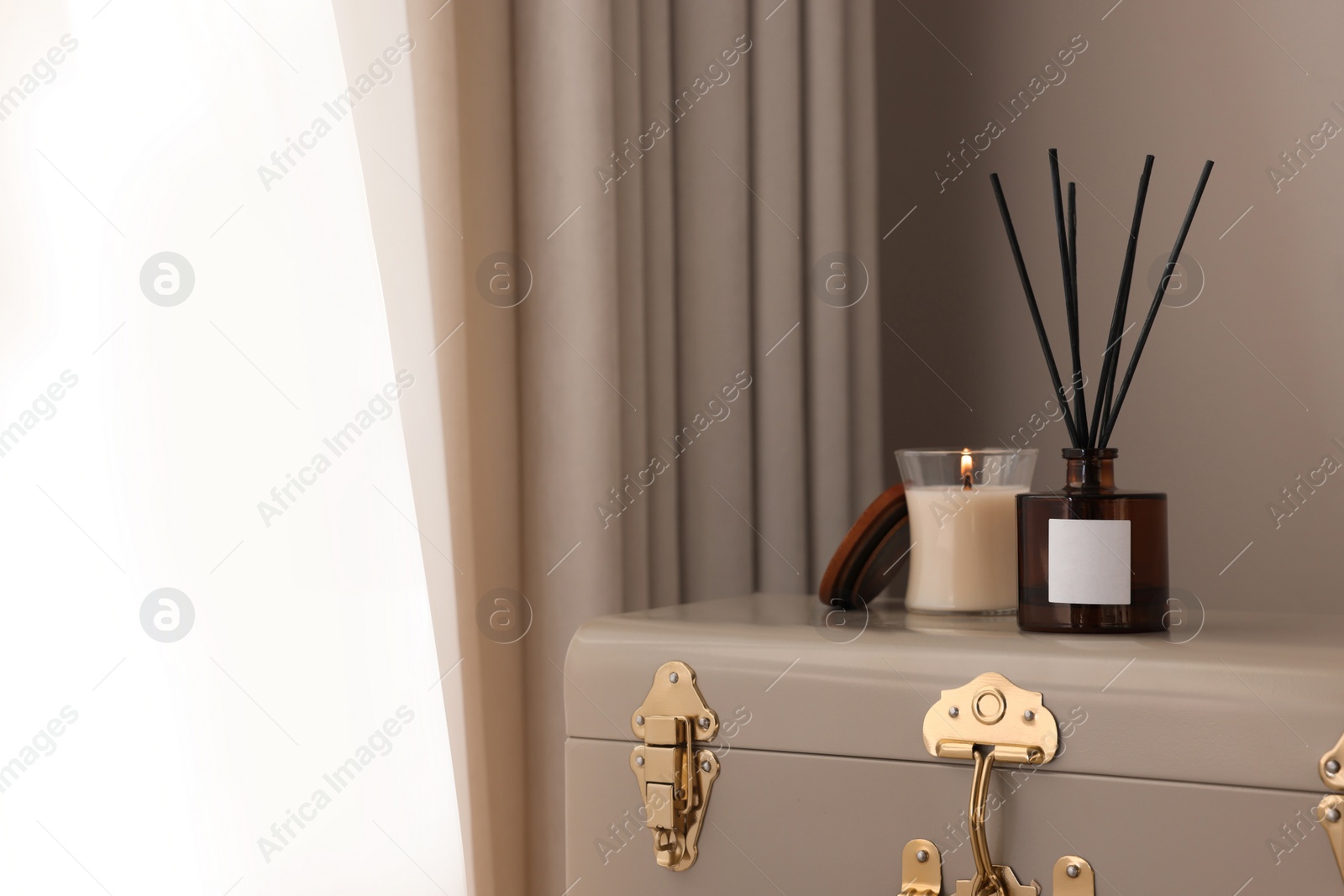 Photo of Aromatic reed air freshener and candle on suitcase indoors, space for text