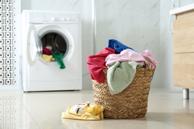 Photo of Wicker laundry basket with different clothes on floor near washing machine in bathroom. Space for text