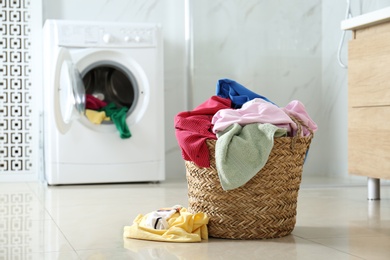 Wicker laundry basket with different clothes on floor near washing machine in bathroom. Space for text