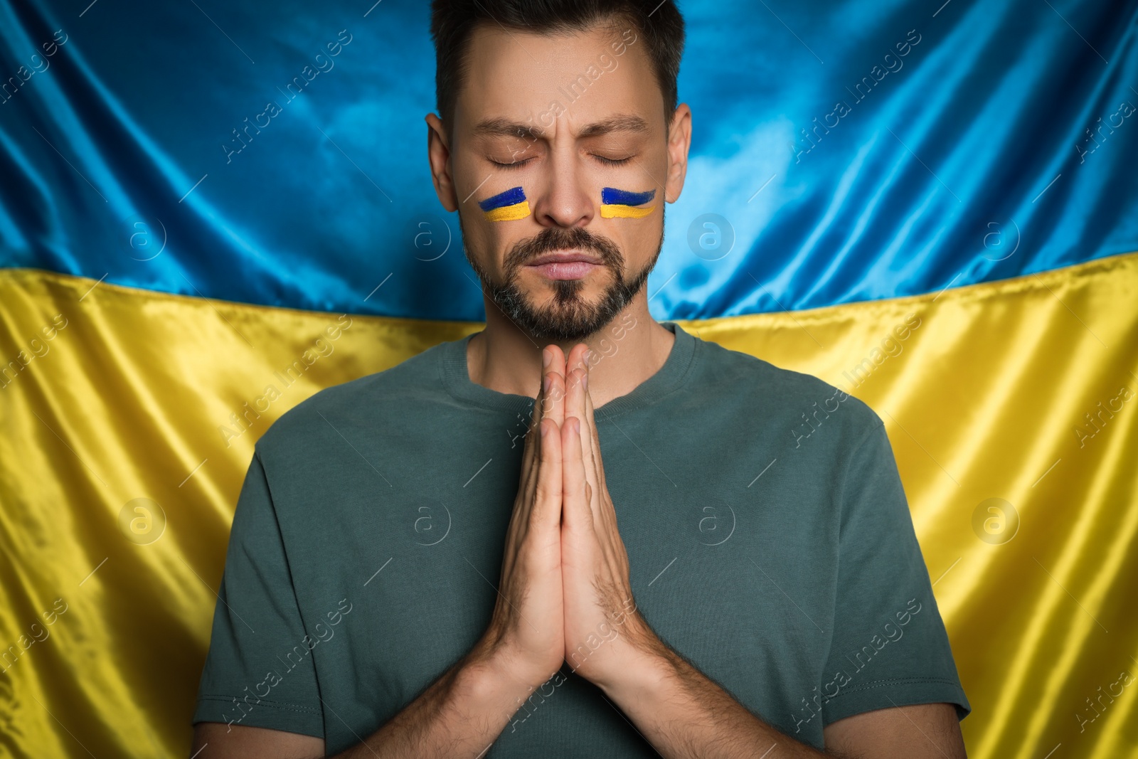 Photo of Man with clasped hands praying near Ukrainian flag