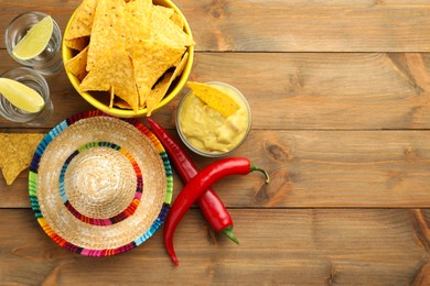 Mexican sombrero hat, tequila, chili peppers, nachos chips and guacamole on wooden table, flat lay. Space for text