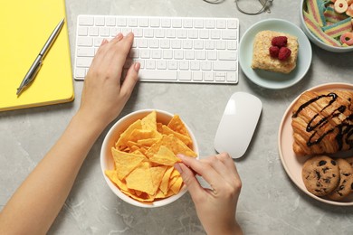 Bad habits. Woman eating different snacks while working on computer at light grey marble table, top view
