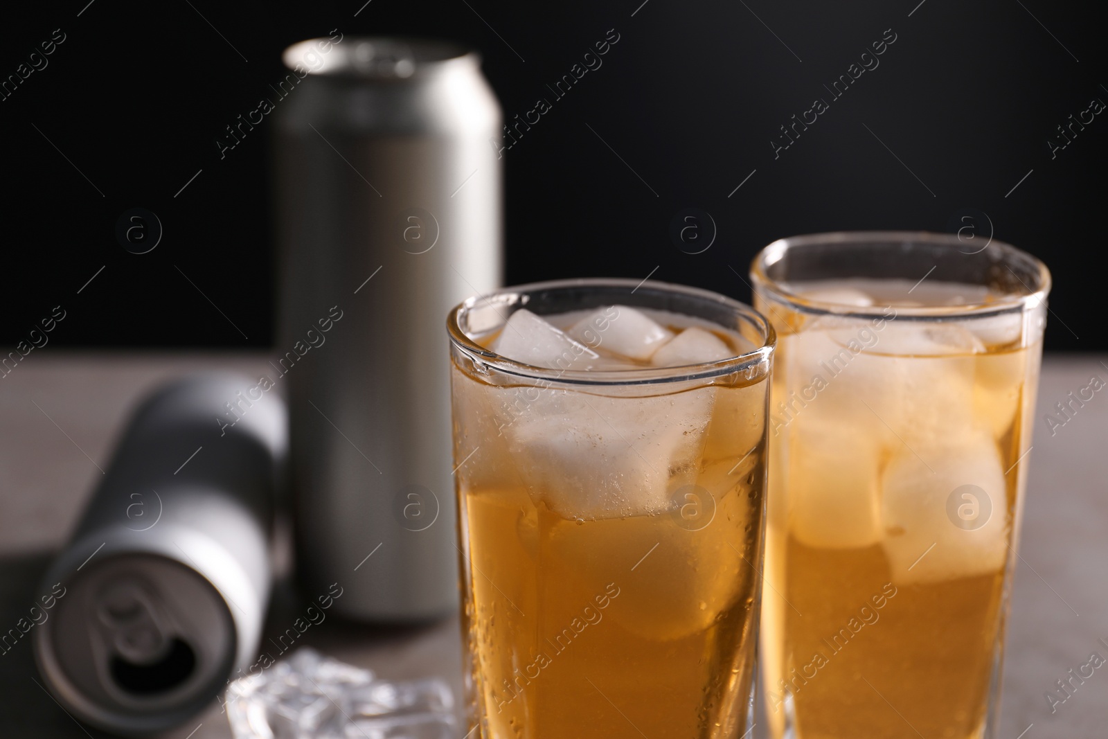 Photo of Energy drink with ice cubes in glasses and aluminium cans on table, closeup