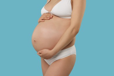 Pregnant woman in stylish comfortable underwear on light blue background, closeup