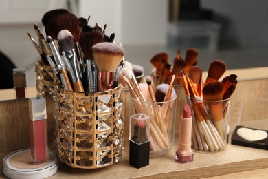 Photo of Set of professional brushes and makeup products near mirror on wooden table