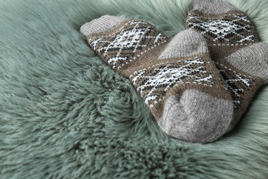 Photo of Knitted socks on grey faux fur, closeup. Space for text