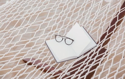 Photo of Comfortable hammock with book and glasses at seaside