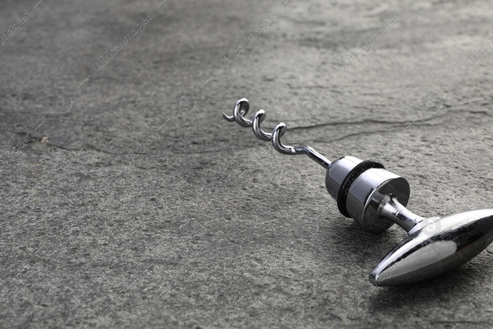 Photo of One metal corkscrew on grey textured table, closeup. Space for text