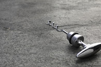 Photo of One metal corkscrew on grey textured table, closeup. Space for text