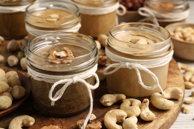 Tasty nut butters in jars and raw nuts on table, closeup