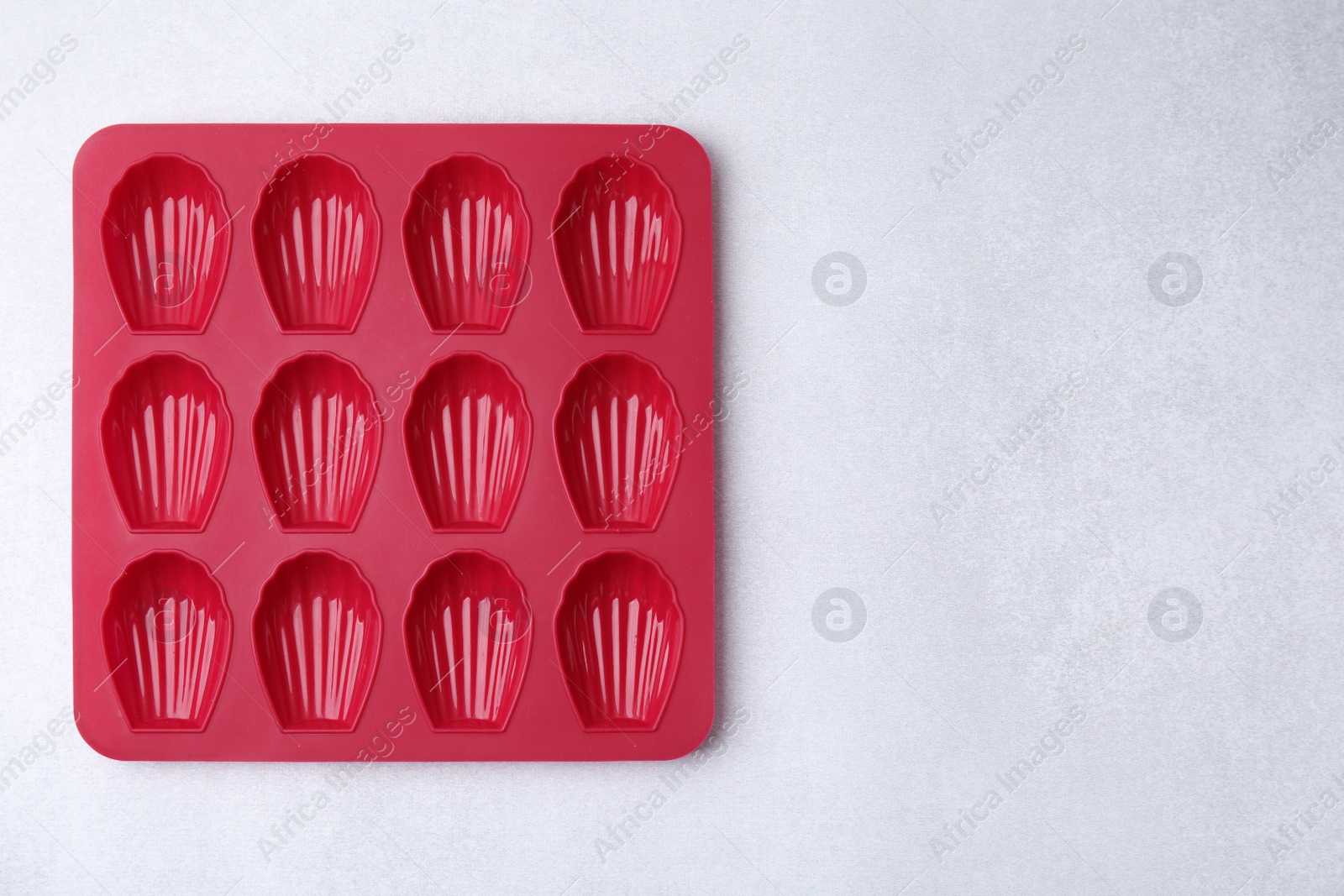 Photo of Red baking mold for madeleine cookies on white table, top view. Space for text