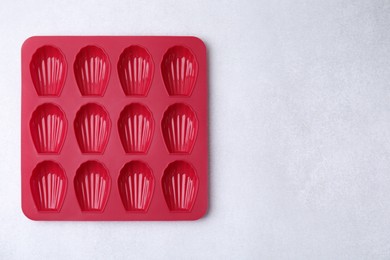 Photo of Red baking mold for madeleine cookies on white table, top view. Space for text