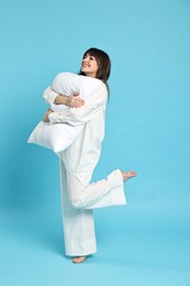 Photo of Happy woman in pyjama holding pillow on light blue background