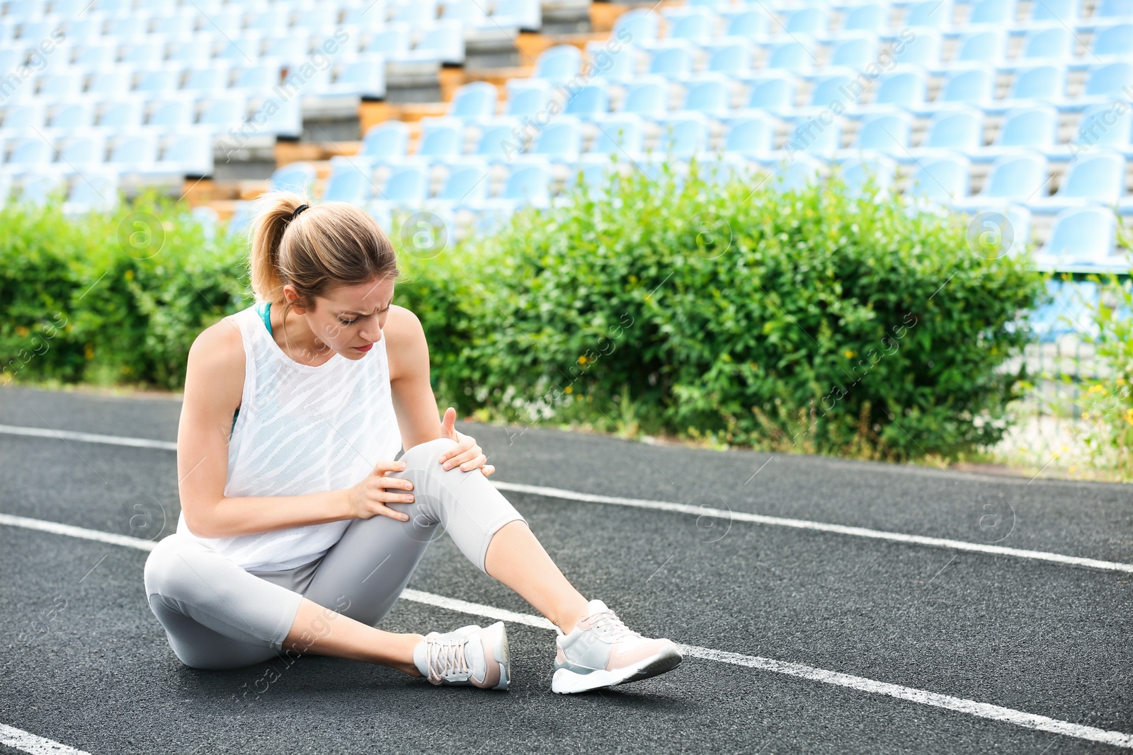 Photo of Woman in sportswear suffering from knee pain at stadium