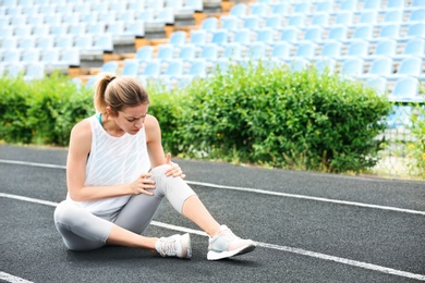 Photo of Woman in sportswear suffering from knee pain at stadium