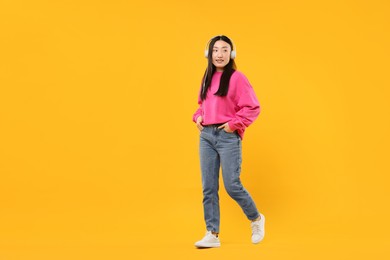 Photo of Portrait of smiling woman in headphones on orange background. Space for text