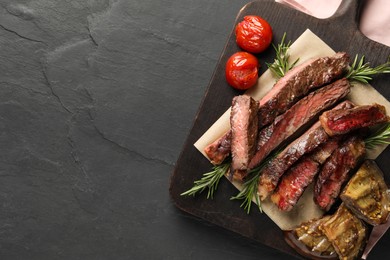 Photo of Delicious grilled beef with vegetables and rosemary on dark gray table, top view. Space for text