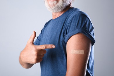 Photo of Senior man pointing at arm with bandage after vaccination on grey background, closeup